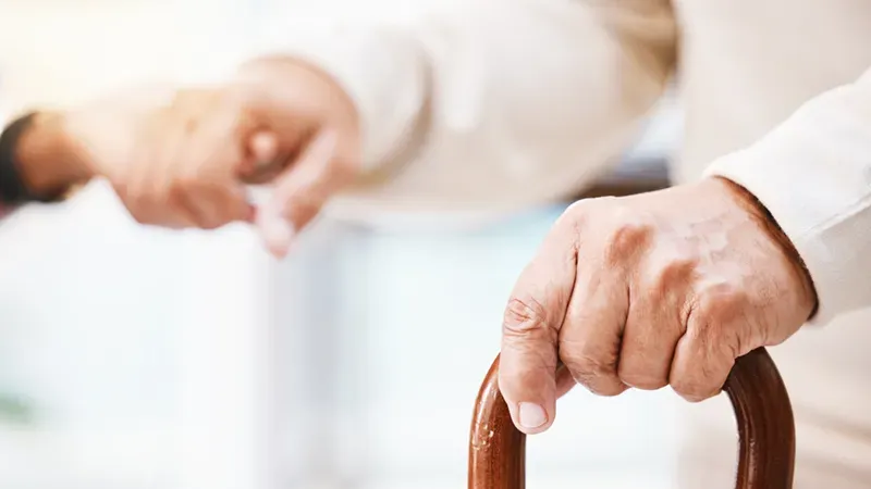 Pflegeperson hält die Hand eines Seniors, der sich auf seinen Gehstock stützt – Unterstützung, die mit oder ohne Pflegegrad in Anspruch genommen werden kann